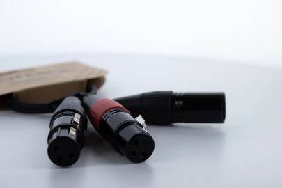 Trois câbles XLR avec une étiquette brune, posés sur un fond blanc, focus sur les extrémités des connecteurs.
