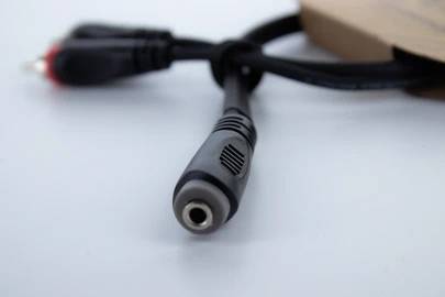 Un câble audio noir avec une fiche jack de 3,5 mm est posé sur un fond blanc et est partiellement inséré dans un emballage en carton.