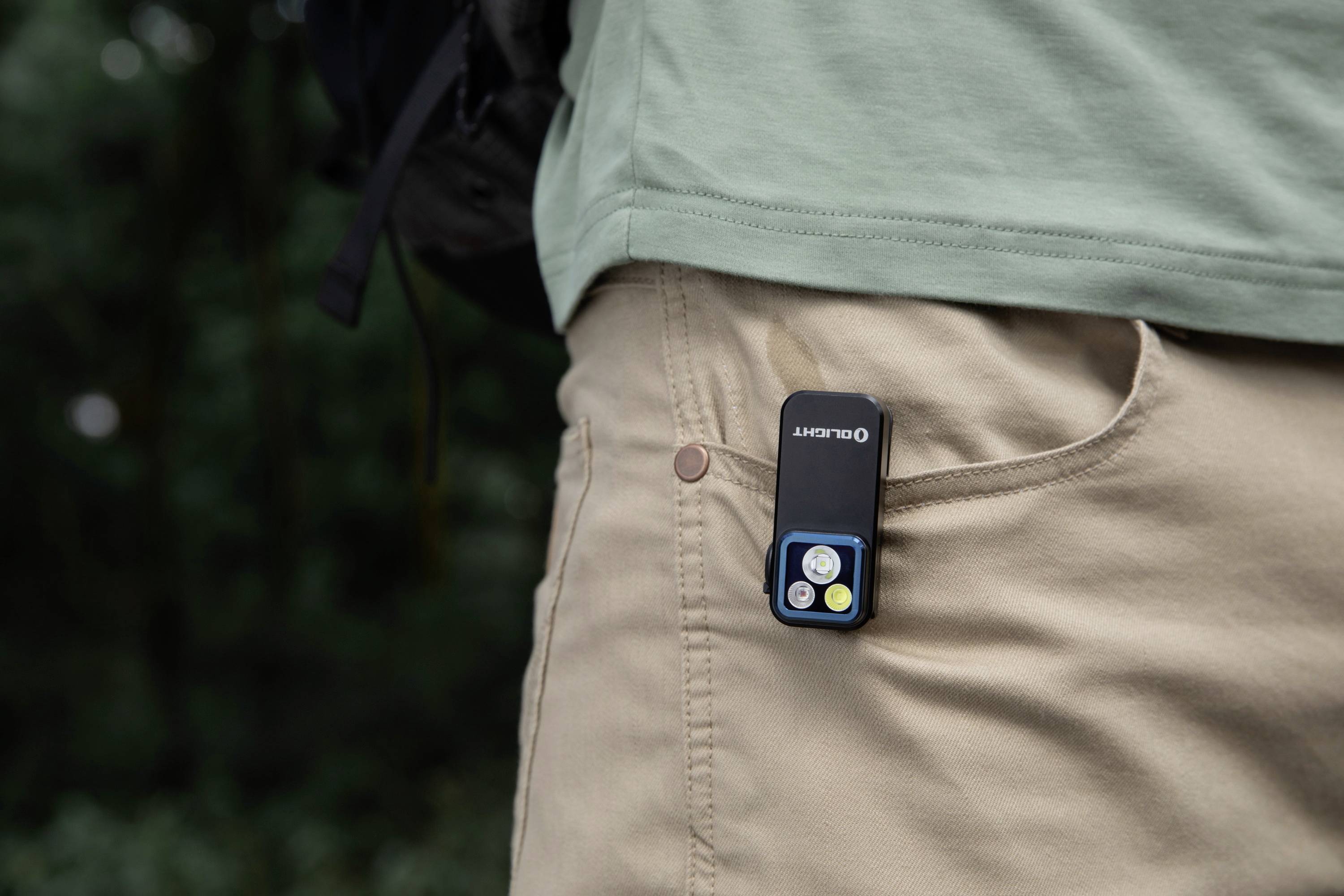 Un petit appareil portable aux touches colorées est glissé dans la poche du pantalon d'une personne portant un t-shirt vert clair.