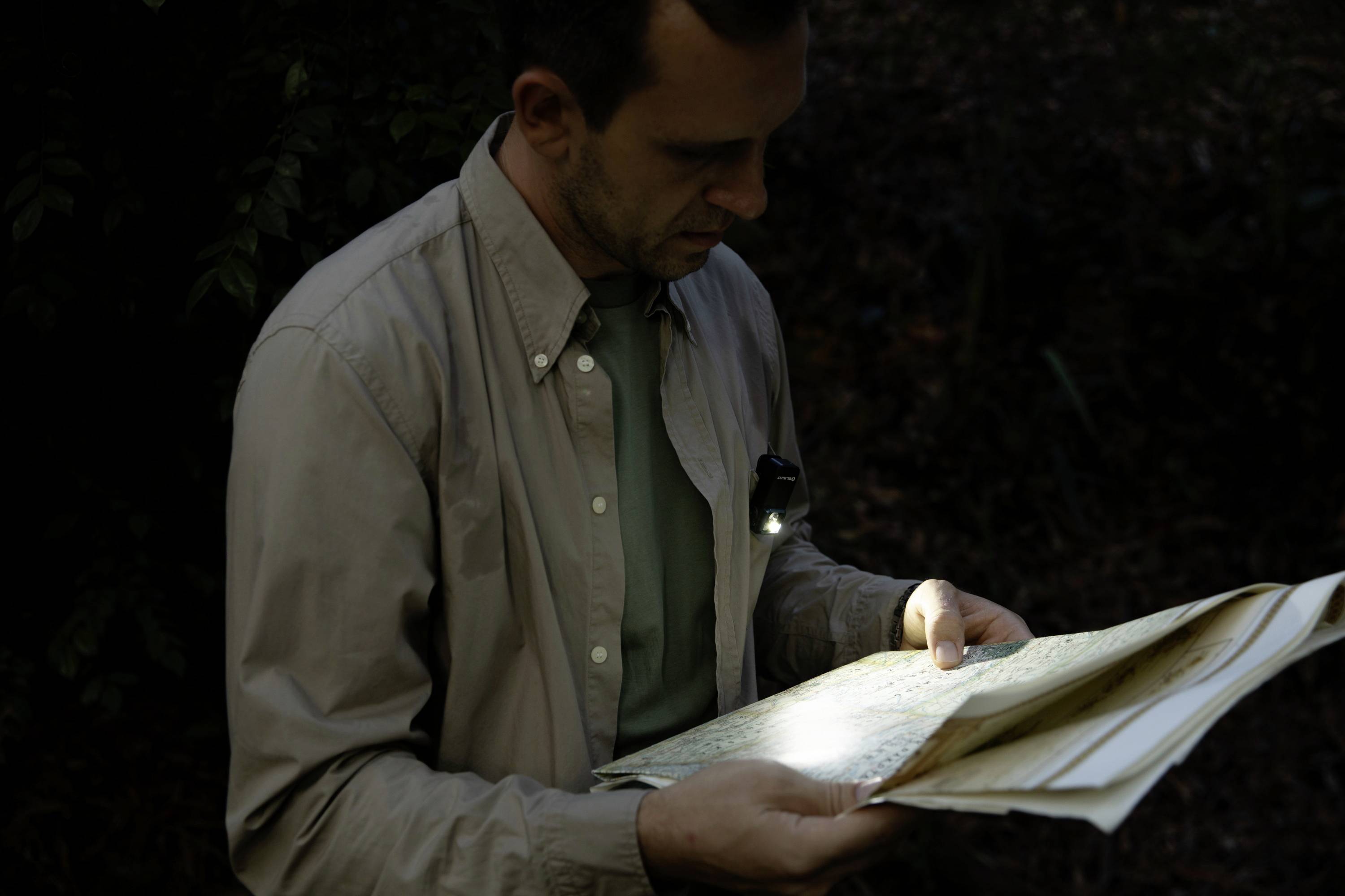 Un homme à l'extérieur, portant une lampe sur sa poitrine, lit un livre dans une faible lumière.