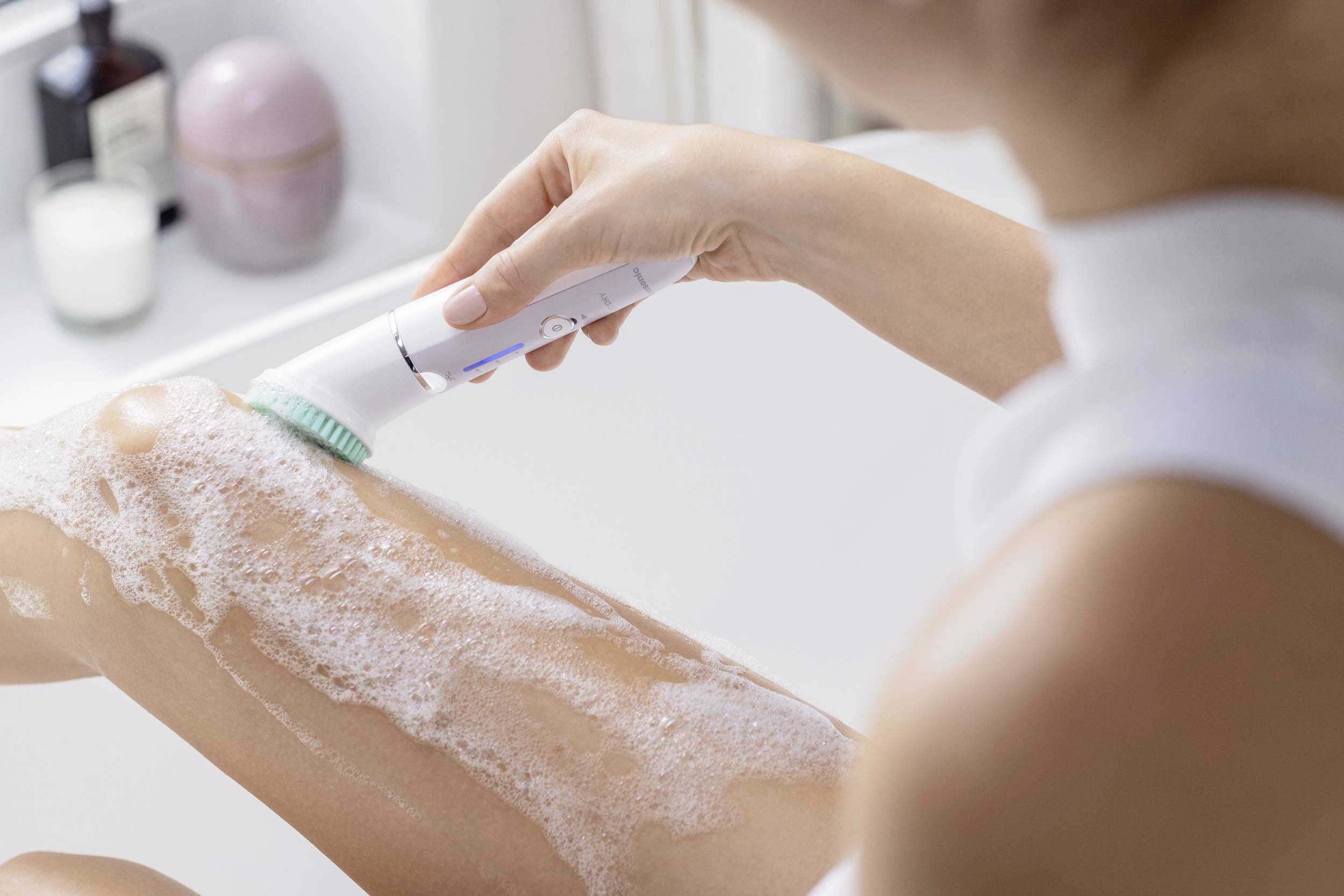 Une personne nettoie une jambe savonnée avec une brosse électrique dans la salle de bain.