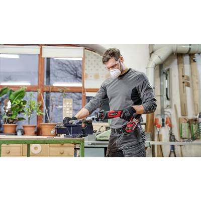 Un homme portant un équipement de protection travaille dans un atelier avec une scie électrique. Des plantes et des outils sont visibles en arrière-plan.