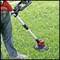 Une personne utilise un coupe-bordure rouge sur une pelouse. Le trimmer possède un long manche et est en action pour couper l'herbe.