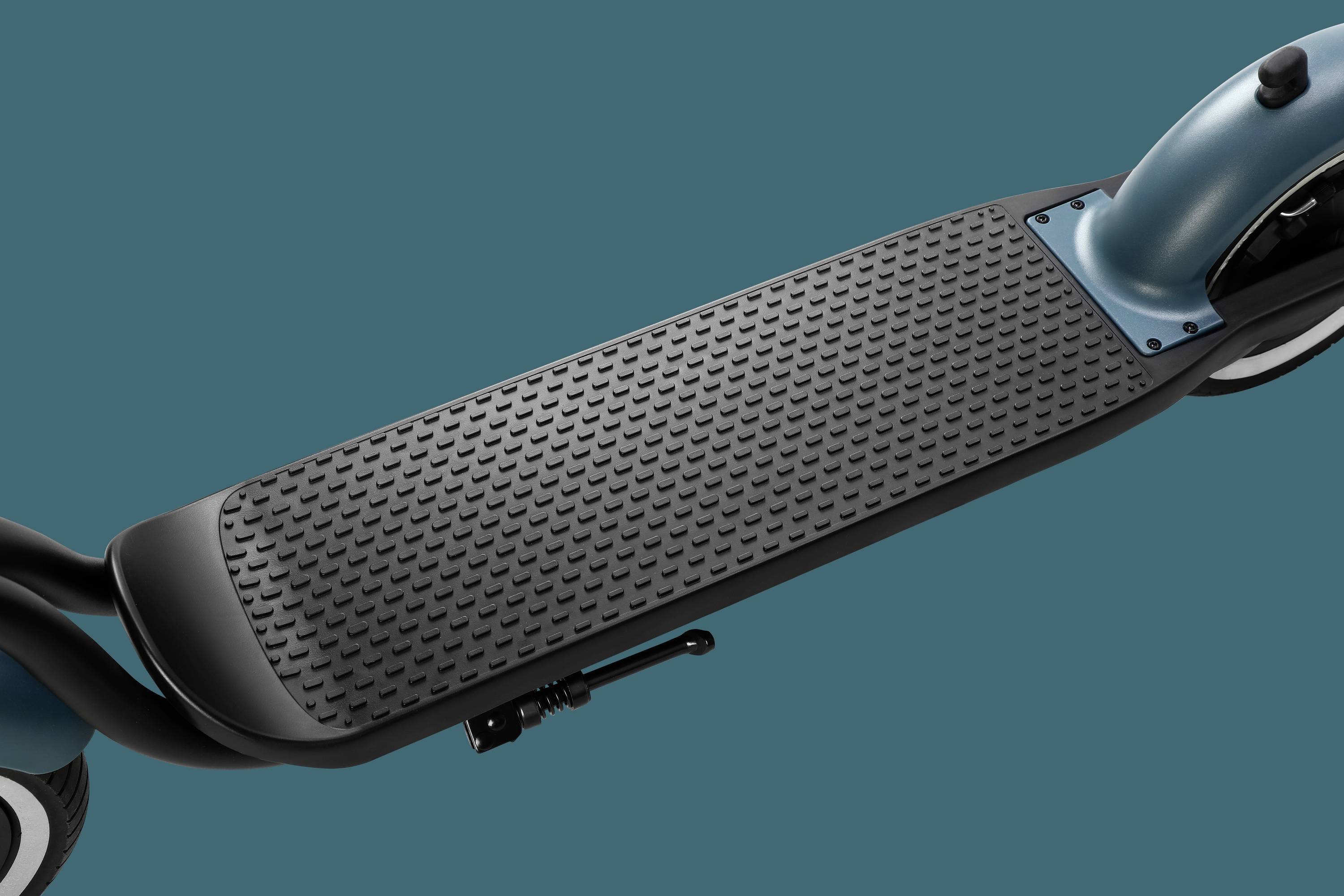 Une planche de trottinette électrique noire sur un fond turquoise, avec une surface antidérapante et un support pliable.