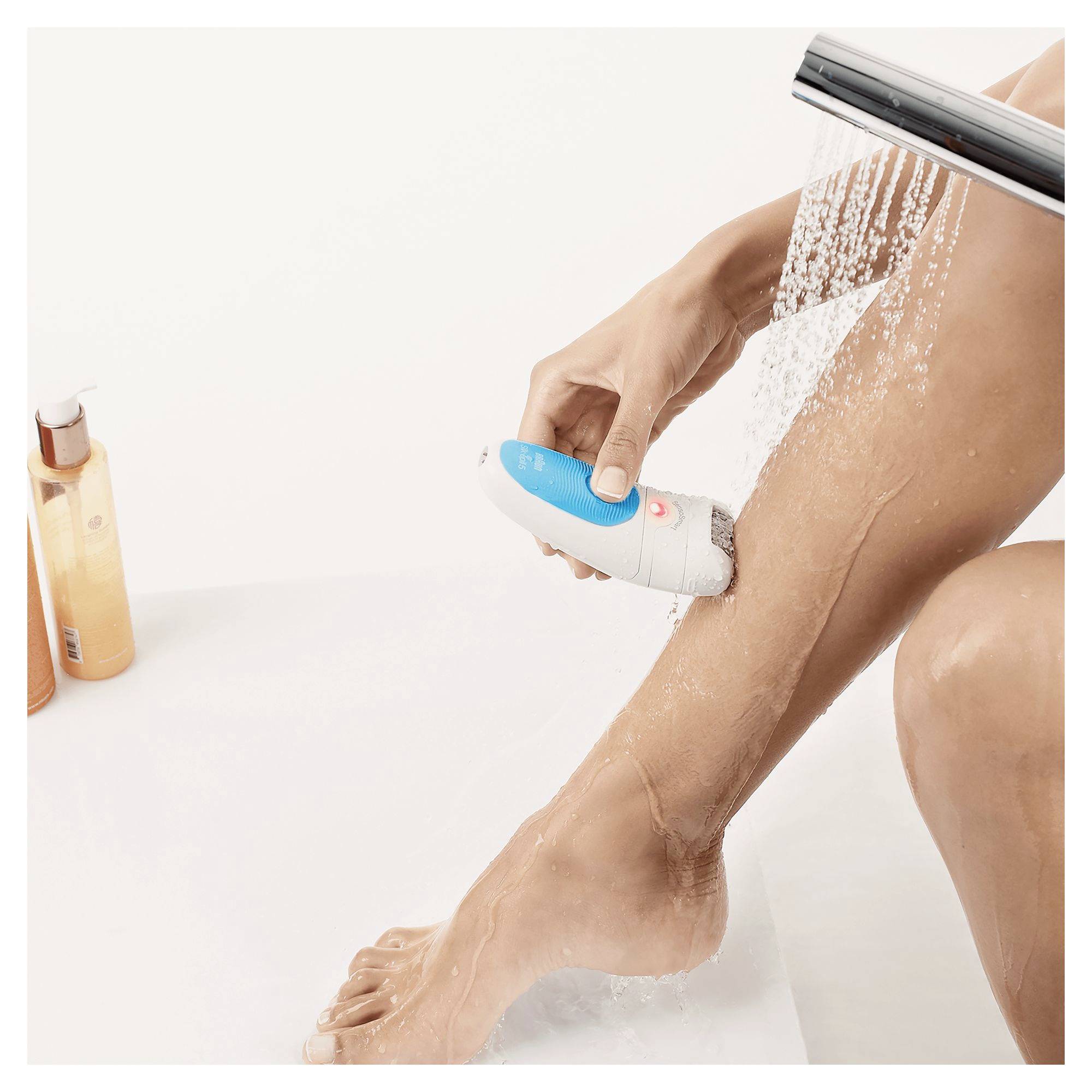 « Une main utilise un épilateur pour épiler la jambe sous un pommeau de douche. Une bouteille de gel douche est posée à côté. »