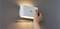 Une main pose un luminaire mural blanc, de forme ovale, sur un support magnétique, démontrant la facilité d'installation. Le texte en allemand indique « magnetische Anbringung ».