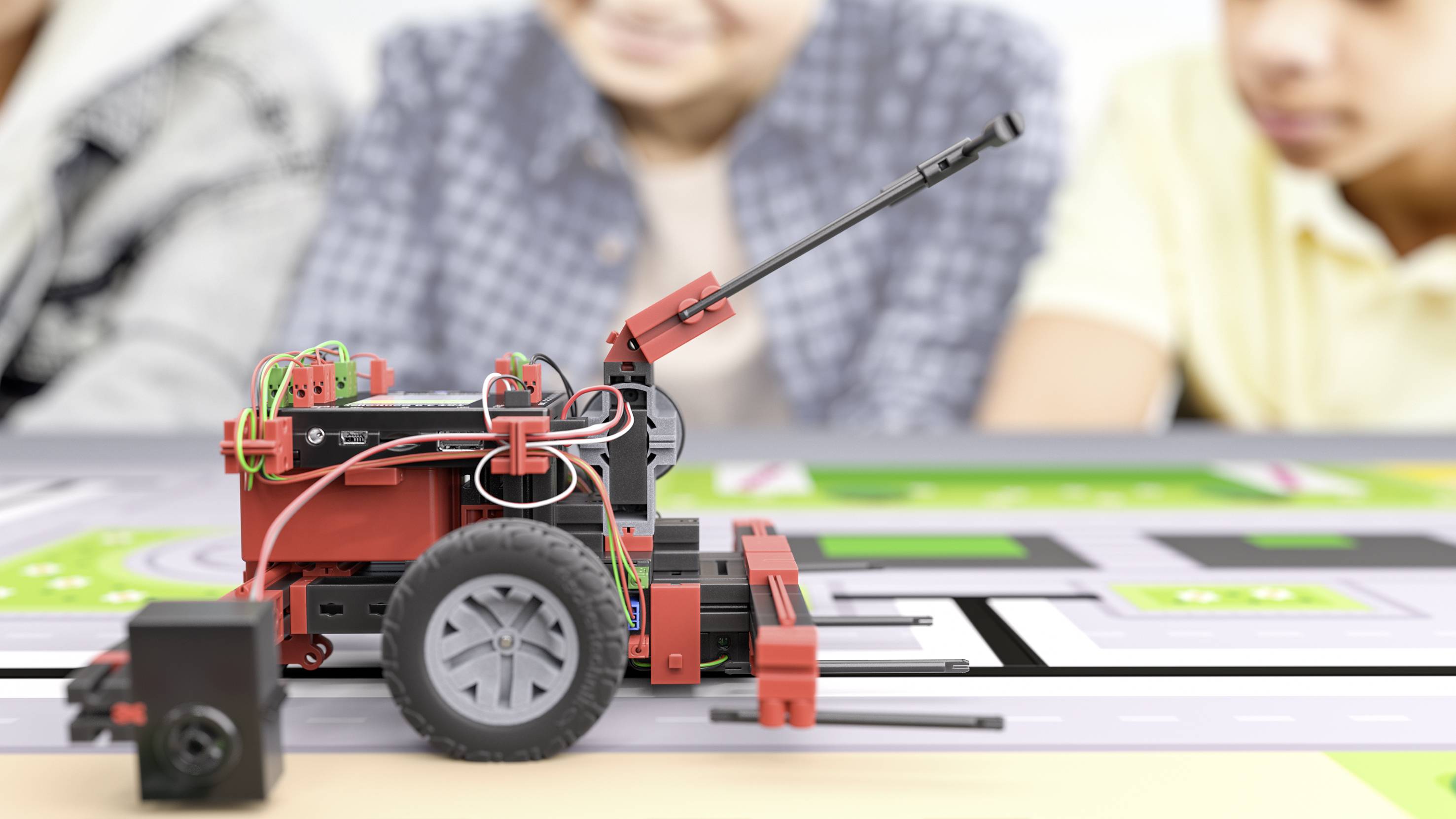 Un véhicule robotique en blocs de construction en gros plan sur une route de jouets, avec des personnes floues en arrière-plan qui regardent.