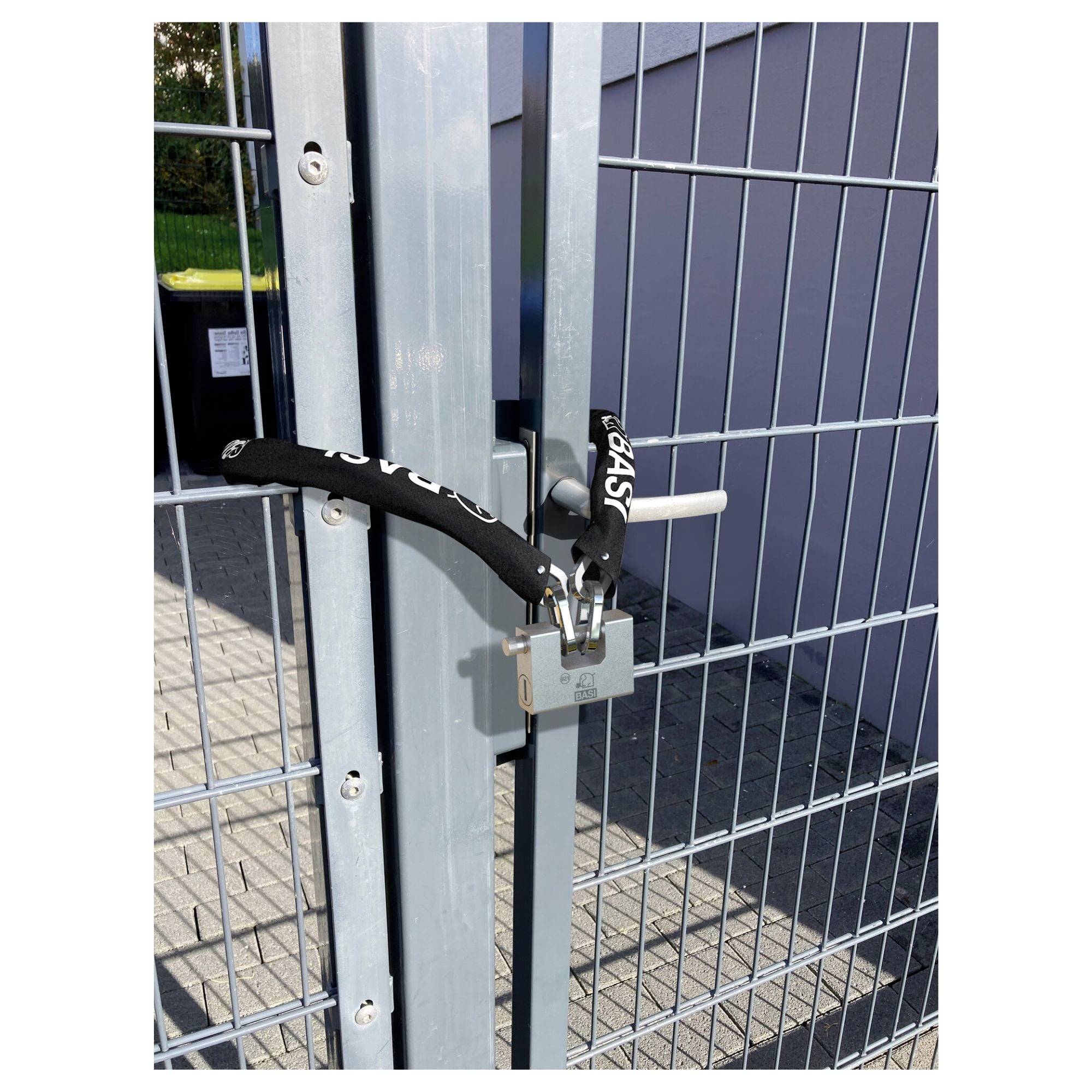 Une grille argentée sécurisée par un cadenas noir. À l'arrière-plan, une poubelle sur une surface pavée.
