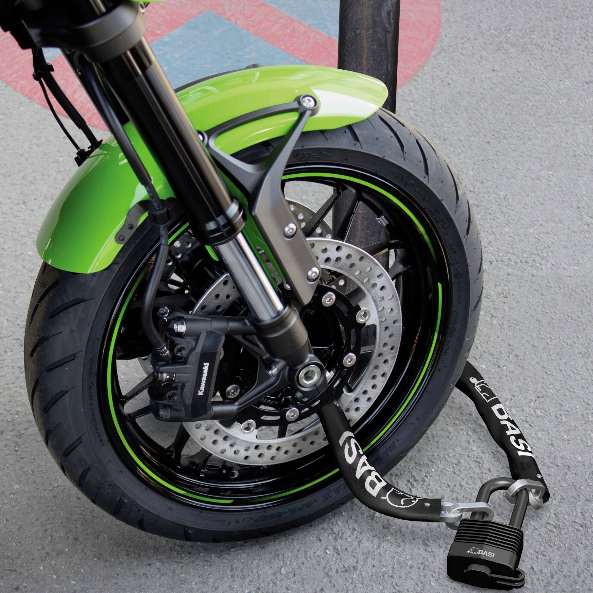 Une moto verte avec un système de freinage puissant est immobile. Un solide antivol sécurise la roue avant sur un trottoir.