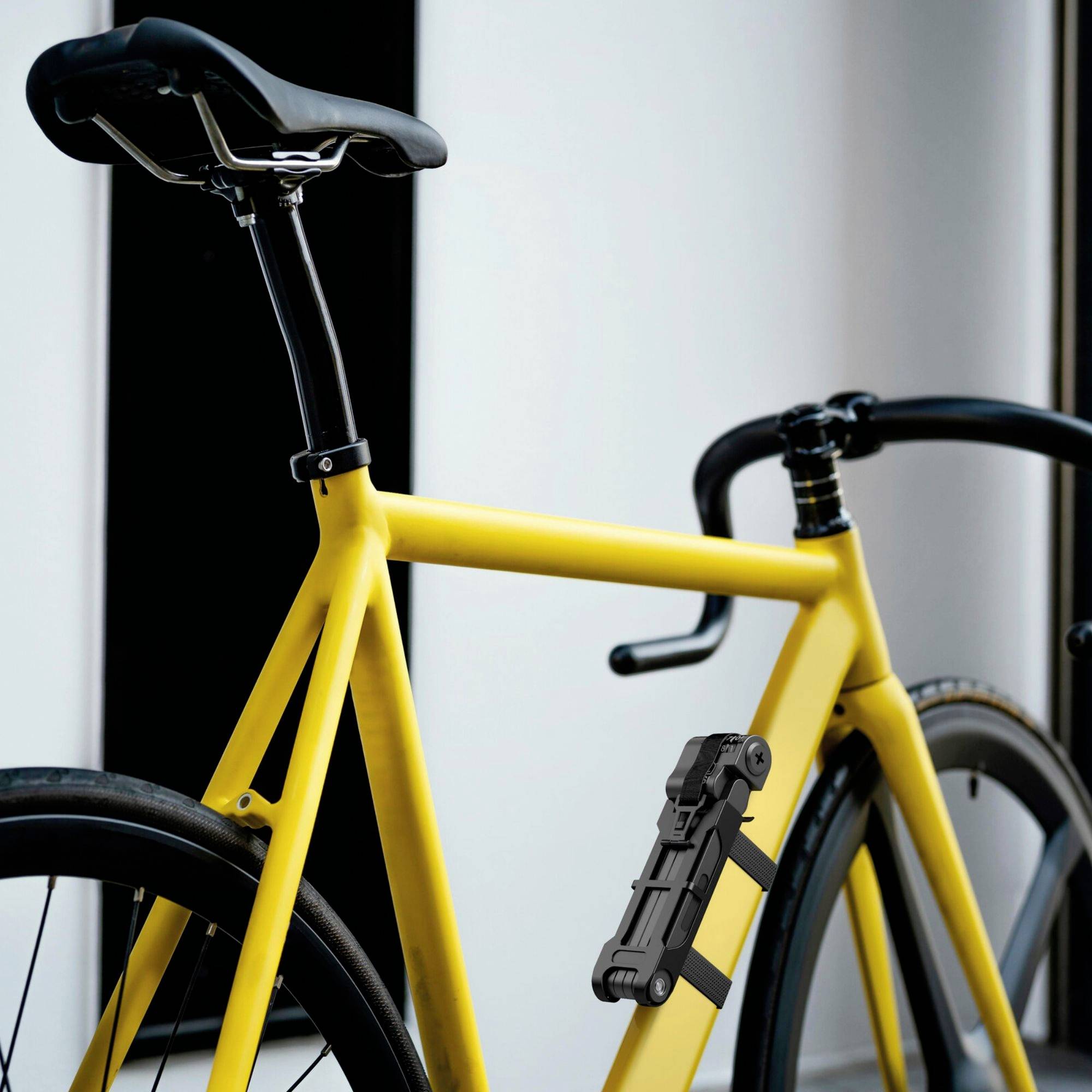 Un vélo de course jaune est posé contre un mur blanc, avec un antivol noir fixé sur le cadre.