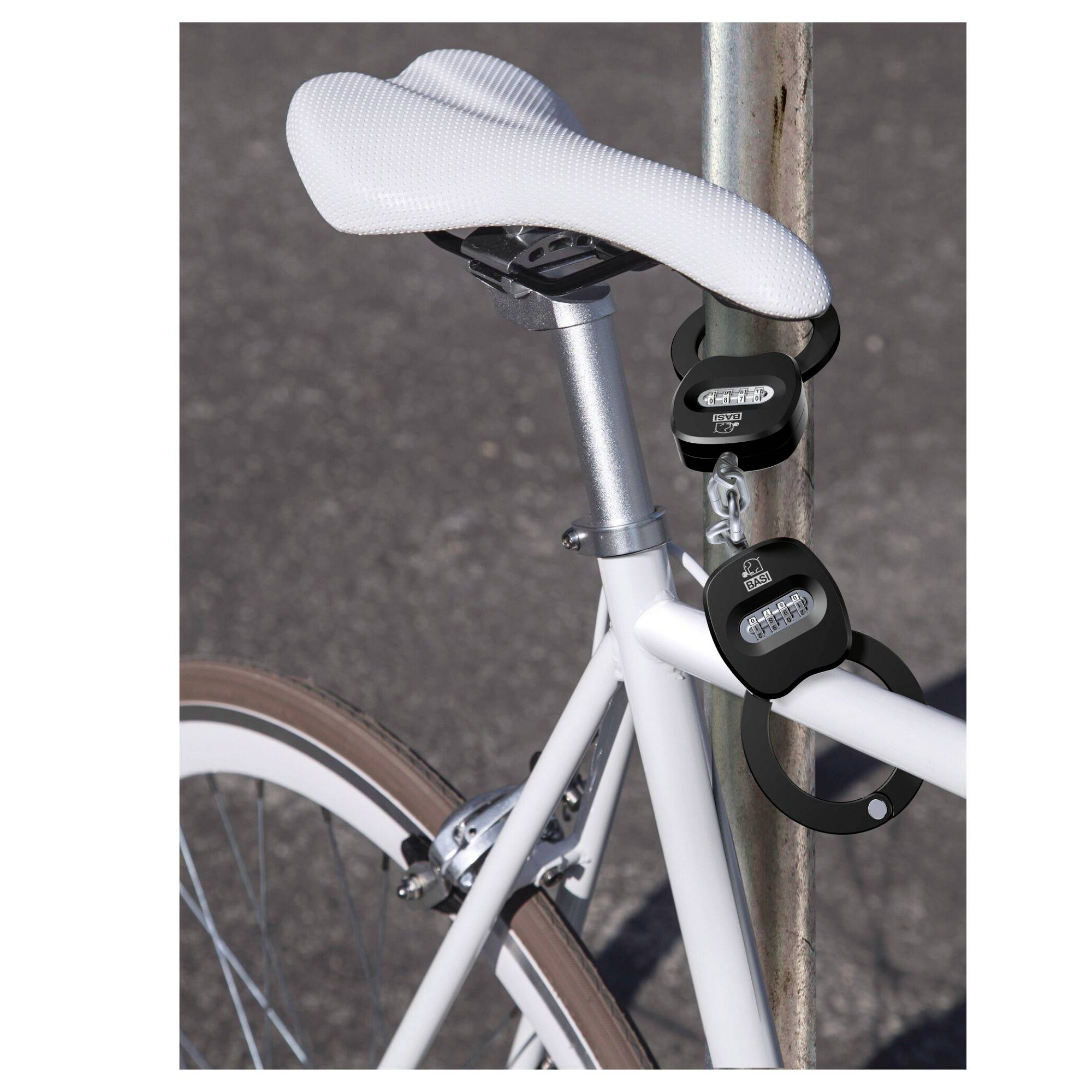 Un vélo blanc est sécurisé avec un antivol à chaîne sur un poteau. La selle est blanche, et le vélo est stationné sur de l'asphalte gris.