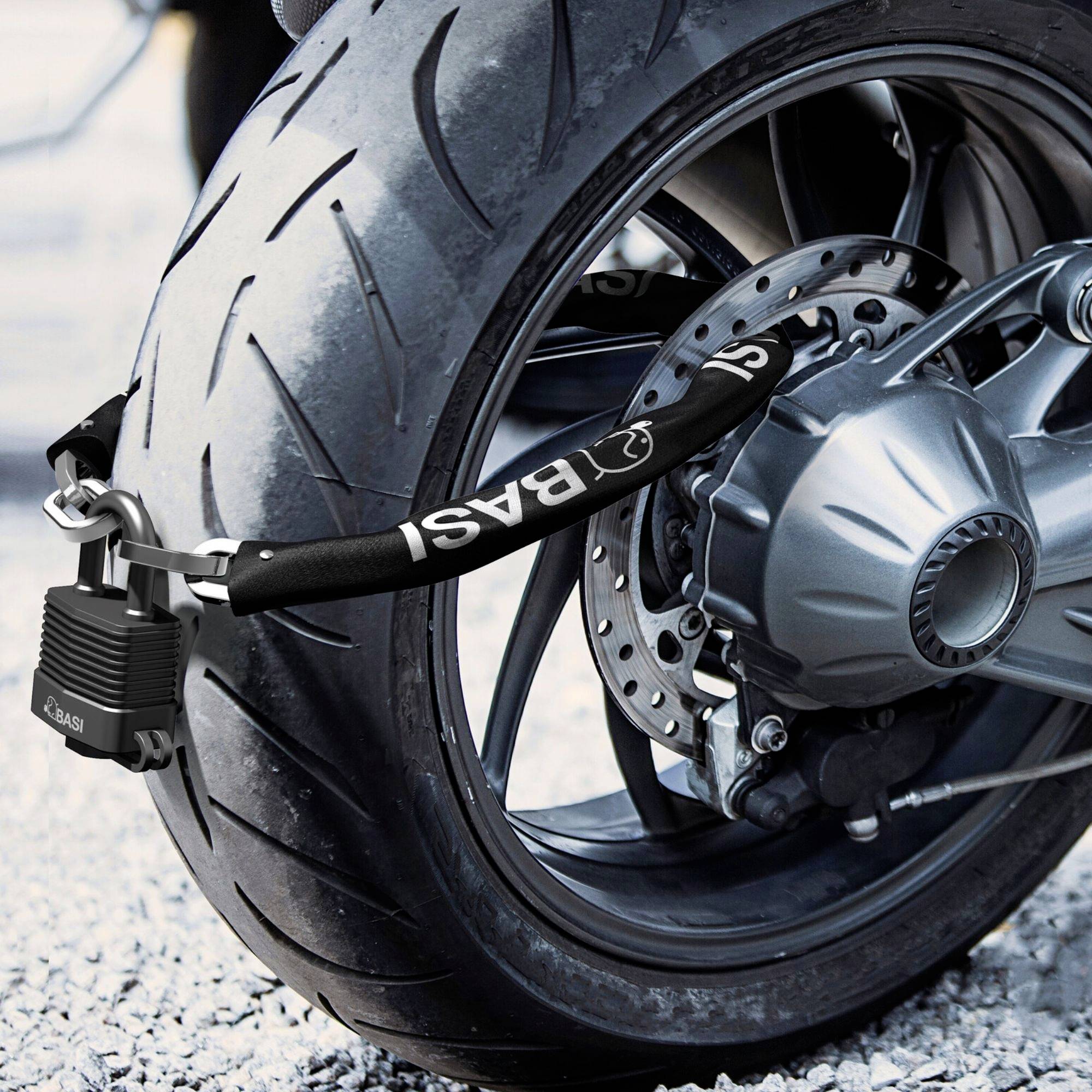 Roue avant d'une moto sécurisée par un épais cadenas noir passant à travers la jante. Environnement avec sol graveleux.