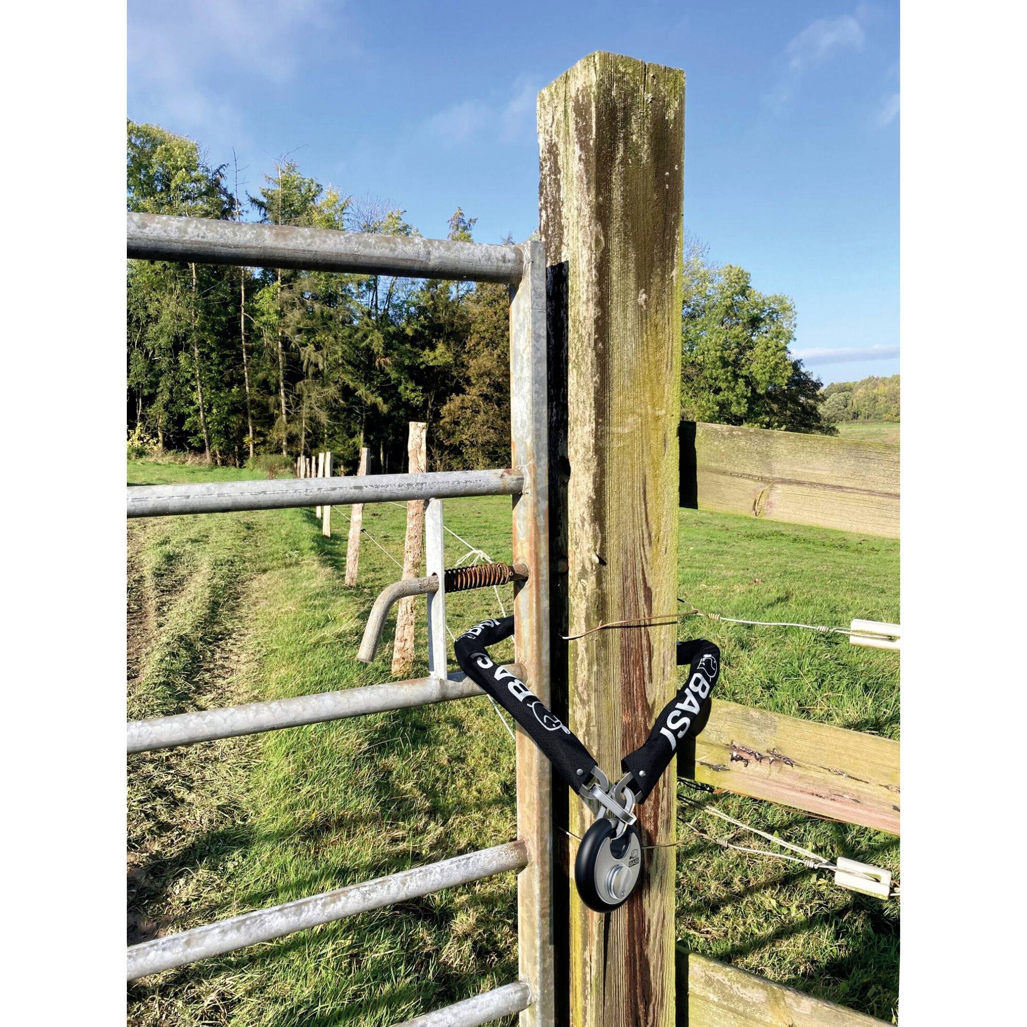 Une grille métallique dans un pré est attachée par une sangle à un poteau en bois. Des arbres et un ciel bleu sont visibles en arrière-plan.
