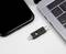 Une clé USB est posée entre un smartphone et un ordinateur portable. La clé dispose de connexions telles que Lightning et USB-C.