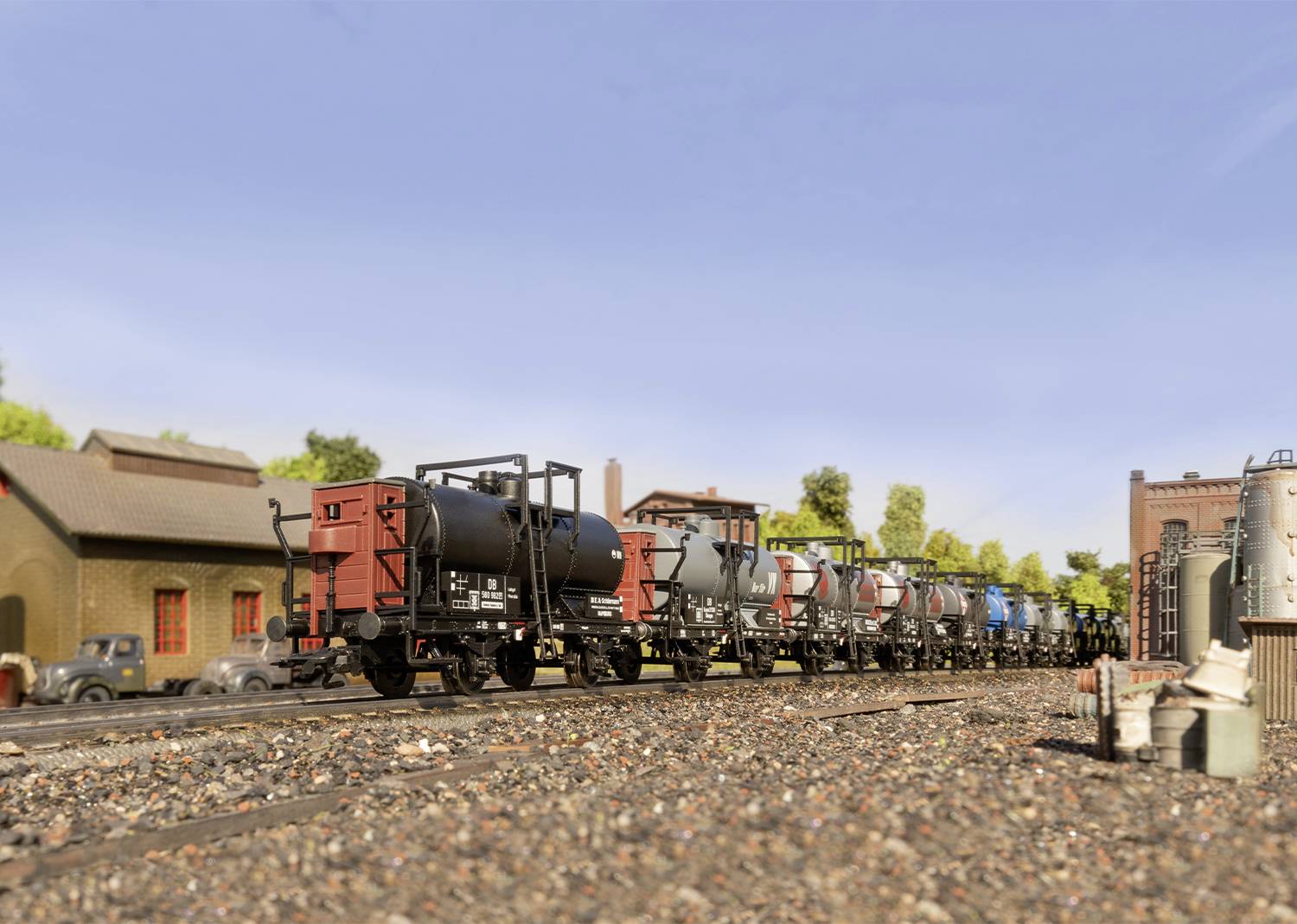 Une rangée de wagons de marchandises miniatures sur des rails près d'une gare miniature, avec des bâtiments et des arbres en arrière-plan sous un ciel dégagé.