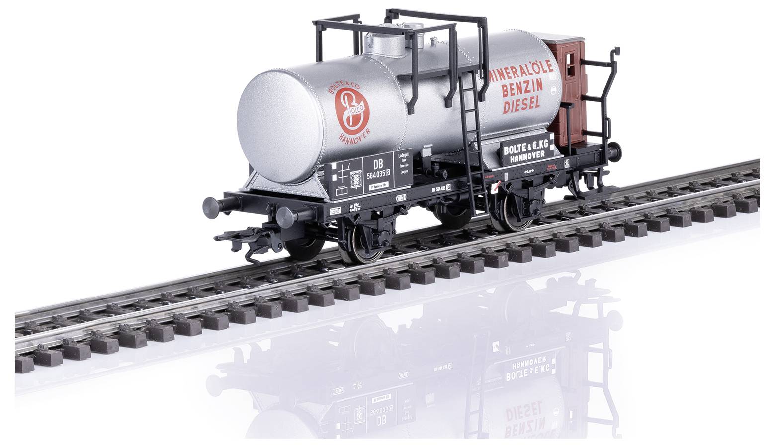 Un wagon de marchandises sur des rails, portant l'inscription 'PÉTROLE ESSENCE DIESEL'. Un réservoir argenté avec une désignation ferroviaire allemande.