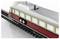 Un train miniature aux couleurs rouge et beige circule sur des rails. La fenêtre sur le côté offre une vue de l'intérieur avec des compartiments à bagages visibles.