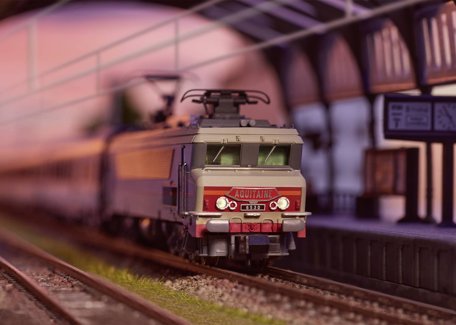 Un train ferroviaire miniature doté de détails précis traverse une scène de gare miniature. La locomotive emblématique 'Aquitaine' conduit le train.