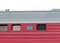 Vue latérale d'une voiture de train rouge, faisant partie d'un train, avec un toit gris et de petites fenêtres. Un panneau bleu avec une inscription est visible.