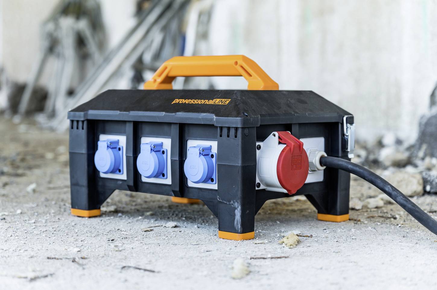 Boîte de distribution électrique avec plusieurs prises et un câble électrique, placée sur un chantier. L'arrière-plan montre des éléments de chantier flous.