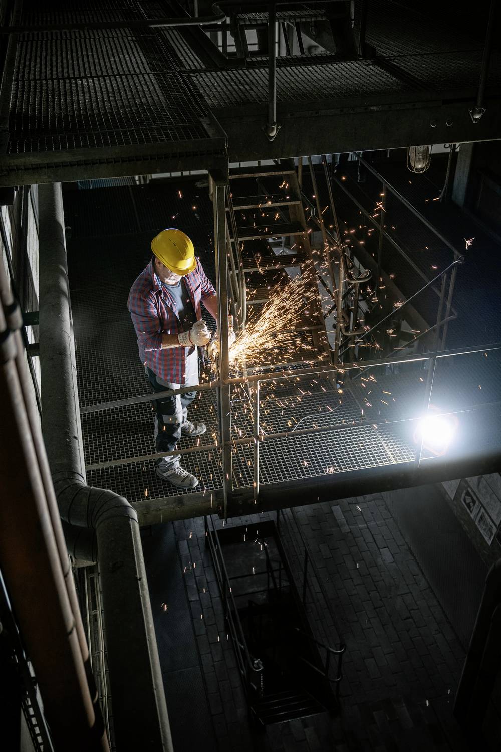 Un ouvrier en tenue de sécurité coupe du métal avec un outil projetant des étincelles dans un environnement industriel sombre.
