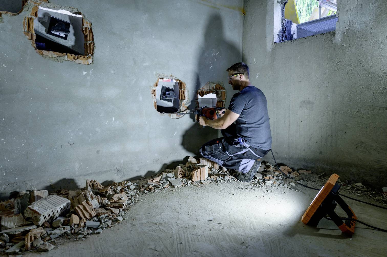 Un artisan travaille sur l'installation de lignes électriques dans un mur inachevé avec des ouvertures de câbles exposées au sous-sol.
