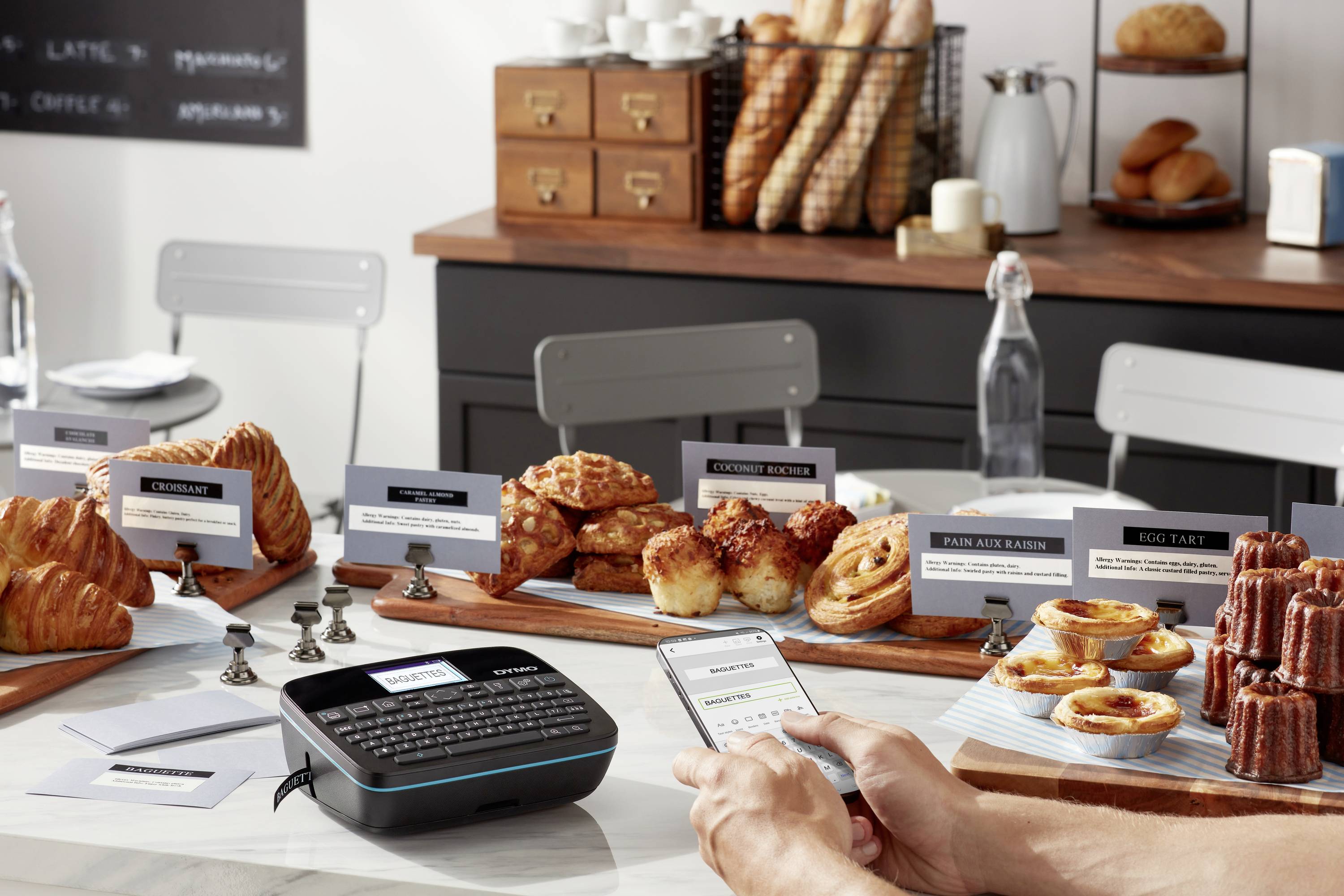 Un café avec une sélection de pâtisseries et de pain sur une table. Une personne utilise un appareil d'étiquetage pour créer des étiquettes de prix.