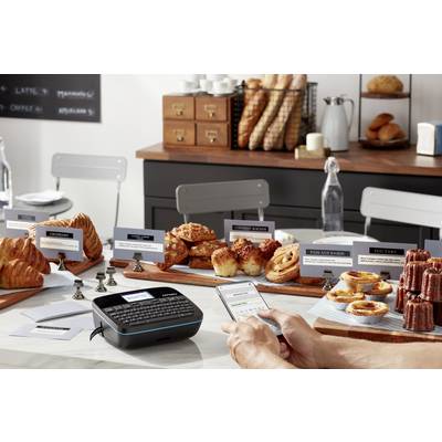 Une personne utilise un appareil d'étiquetage pour créer des étiquettes de prix pour des produits de boulangerie dans une boulangerie. Des pains et des pâtisseries sont visibles en arrière-plan.