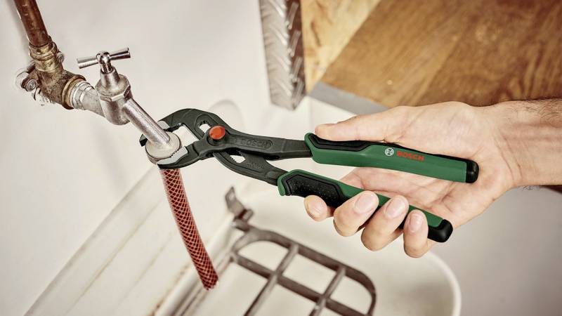 Une main utilise une clé à molette pour serrer un tuyau sous un lavabo. La clé a une poignée verte.