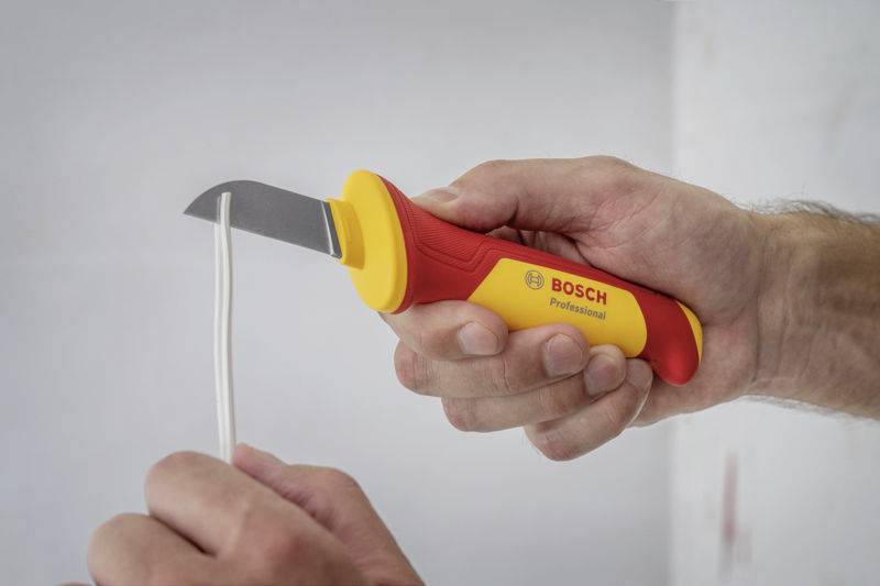 Une personne coupe un câble avec un couteau-câble Bosch Professional. Le couteau a une poignée jaune avec un accent rouge.