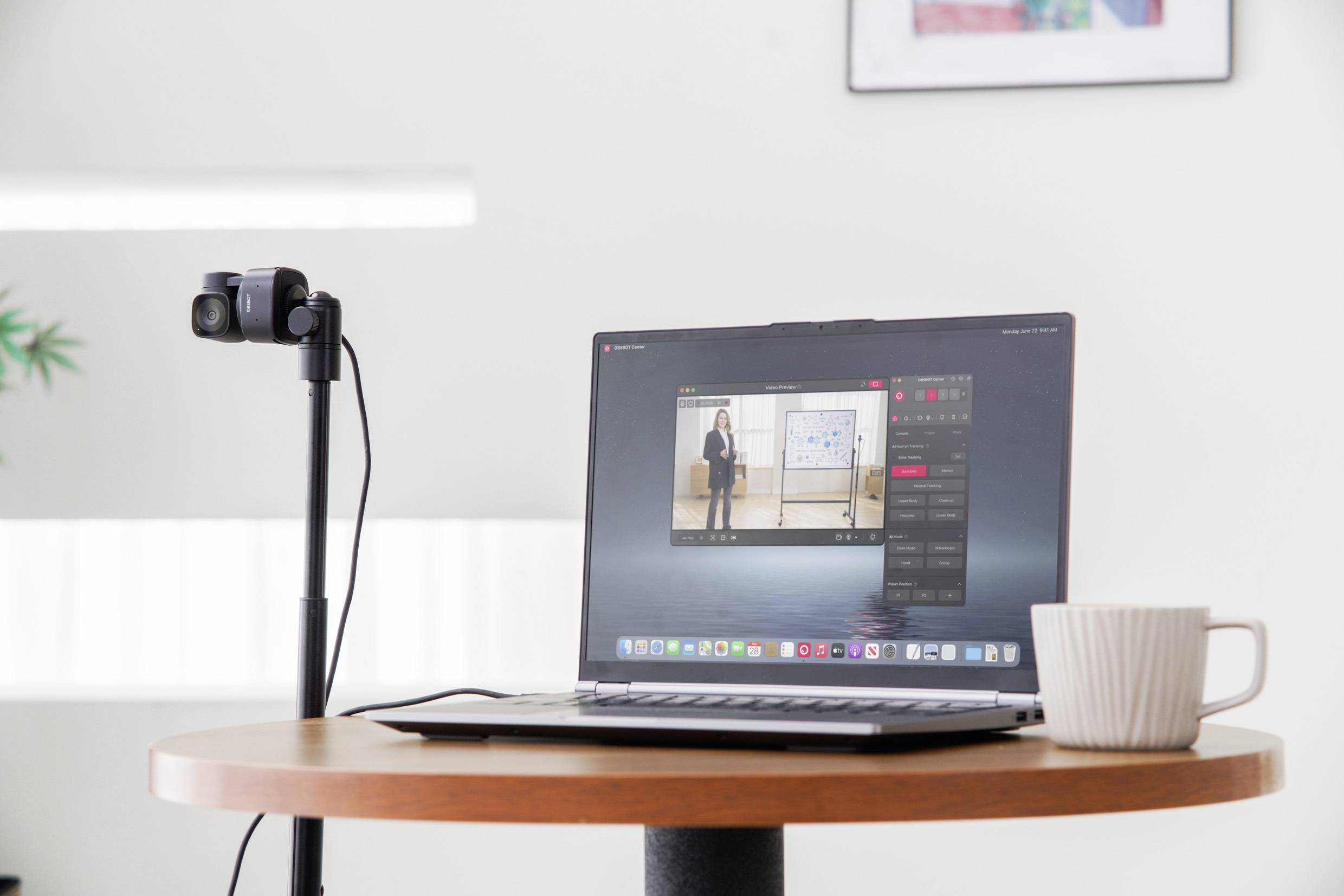 Un ordinateur portable sur une table affiche une présentation sur son écran. À côté, un appareil photo est installé sur un trépied. Une tasse blanche se trouve à proximité.
