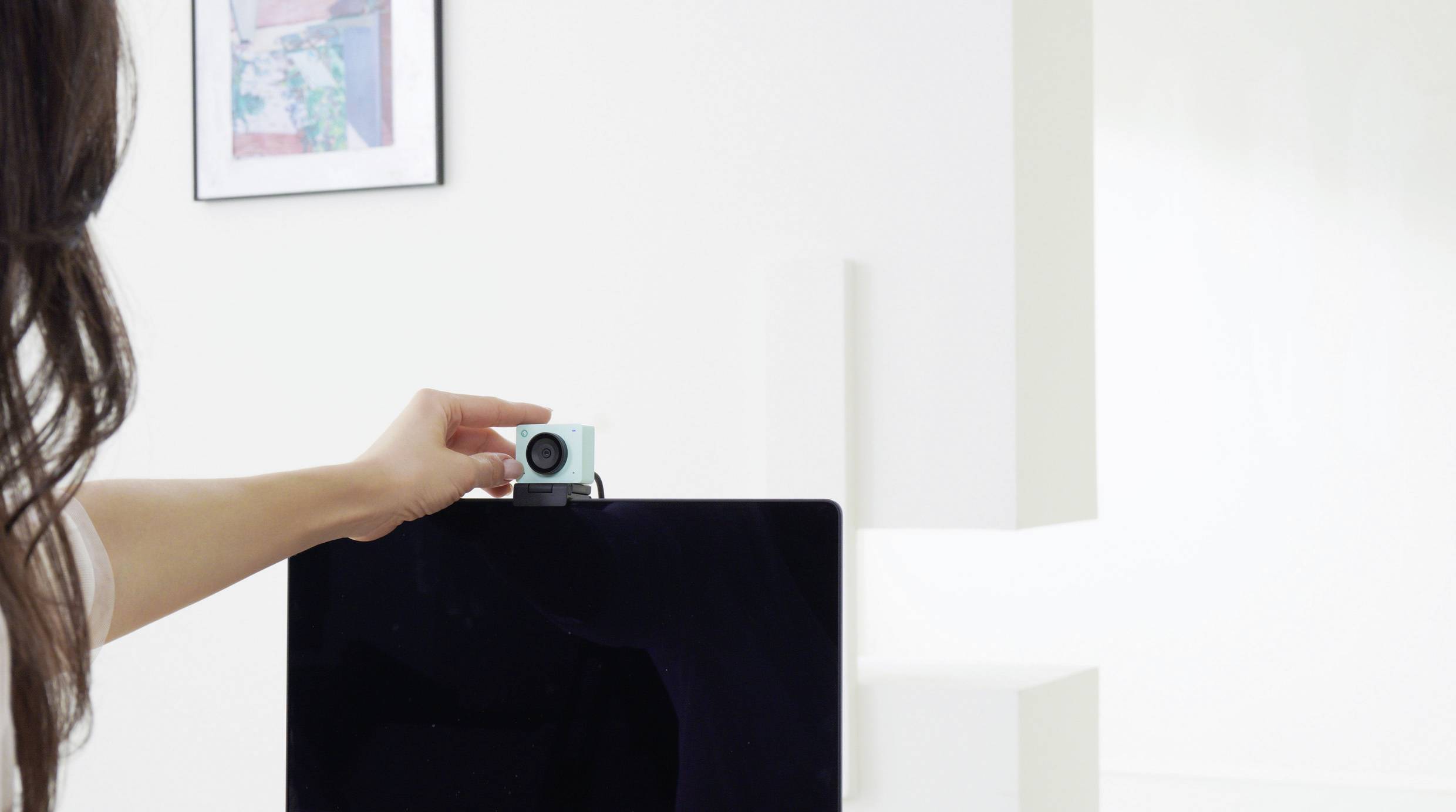 Une personne place une petite caméra en haut d'un écran d'ordinateur dans une pièce au design minimaliste.