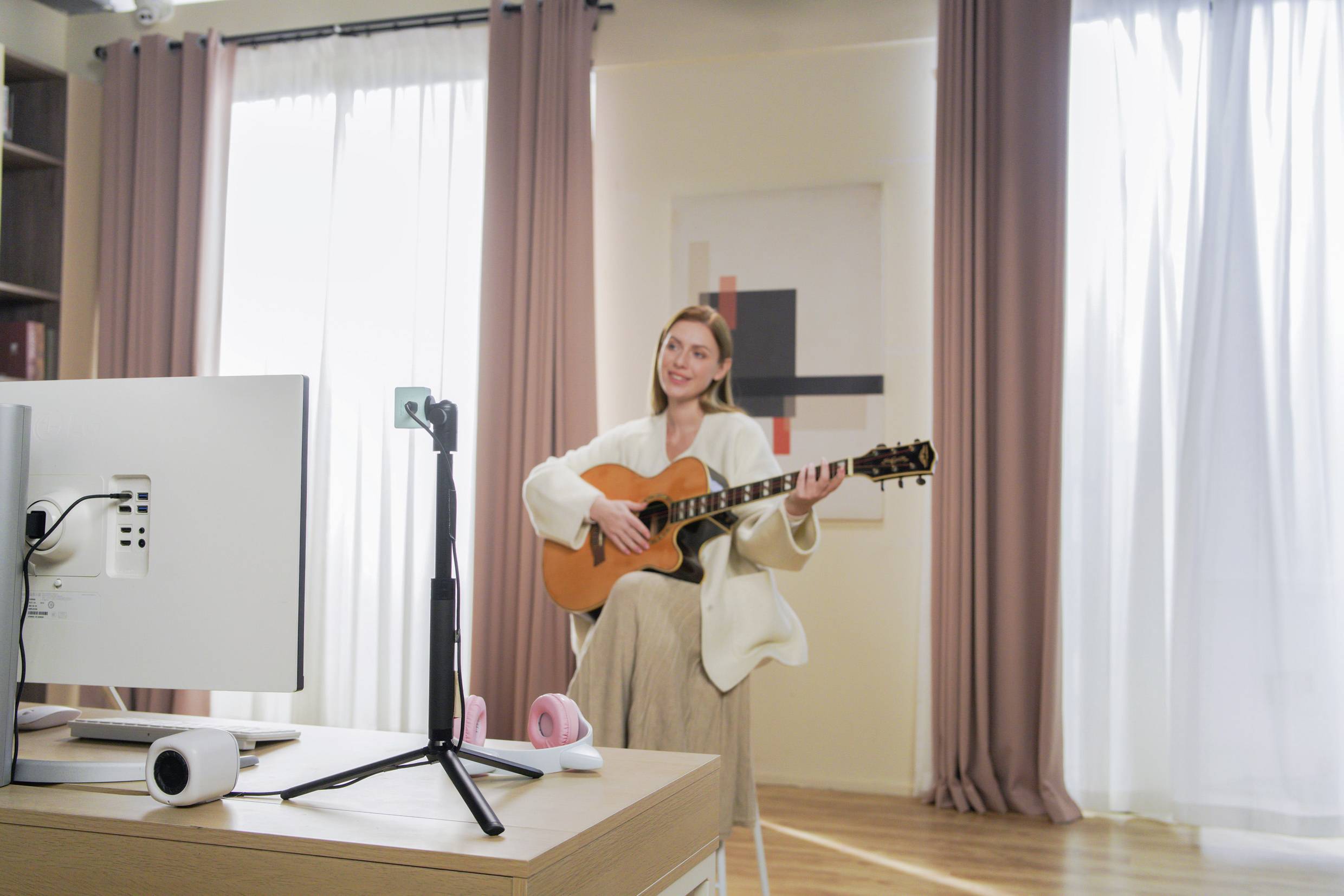 Une personne est assise dans une pièce lumineuse et joue de la guitare devant une caméra sur trépied, ce qui suggère un streaming en ligne.