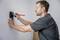 Un homme utilise un appareil de mesure électronique et un stylo rouge sur un mur blanc, probablement pour aligner ou percer.