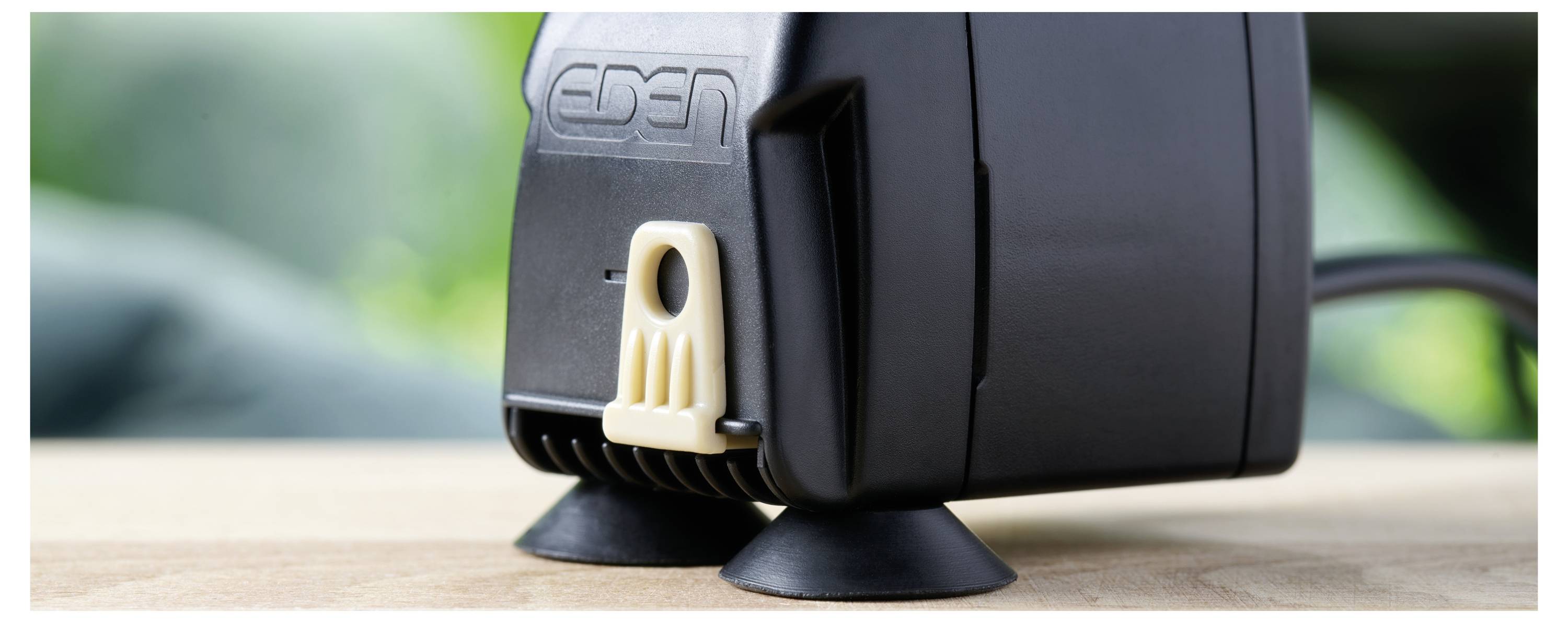 Une pompe à air compacte noire avec des ventouses et un logo 'EDEN', reposant sur une surface en bois, convenant à une utilisation aquariophile.