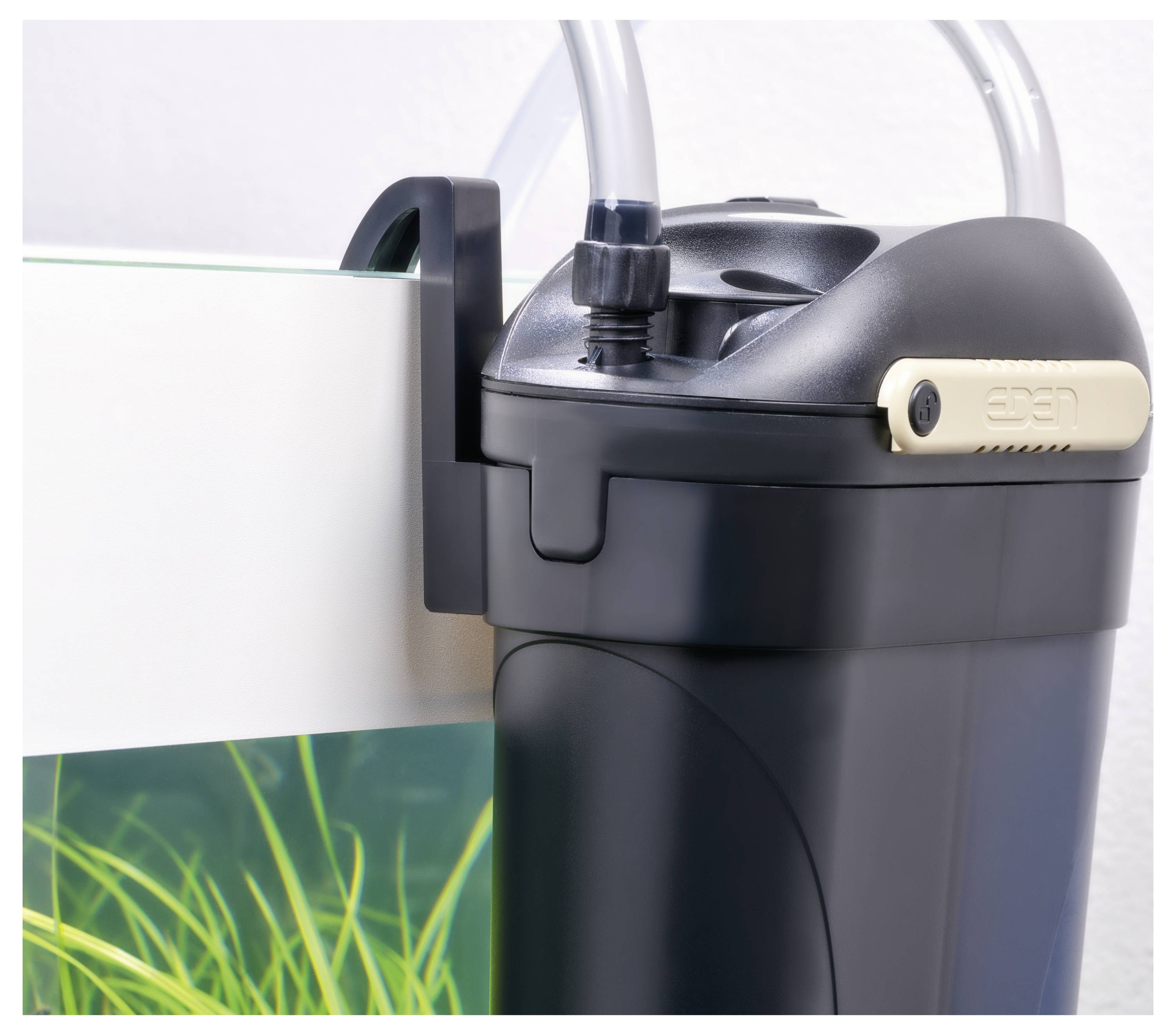 Un filtre à aquarium en canister noir fixé sur le côté d'un réservoir de poissons, avec des tubes pour la filtration de l'eau. Eau claire avec des plantes vertes à l'intérieur de l'aquarium.