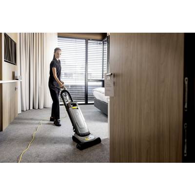 Une personne aspire le tapis avec un aspirateur dans une pièce moderne avec une grande fenêtre et des rideaux.