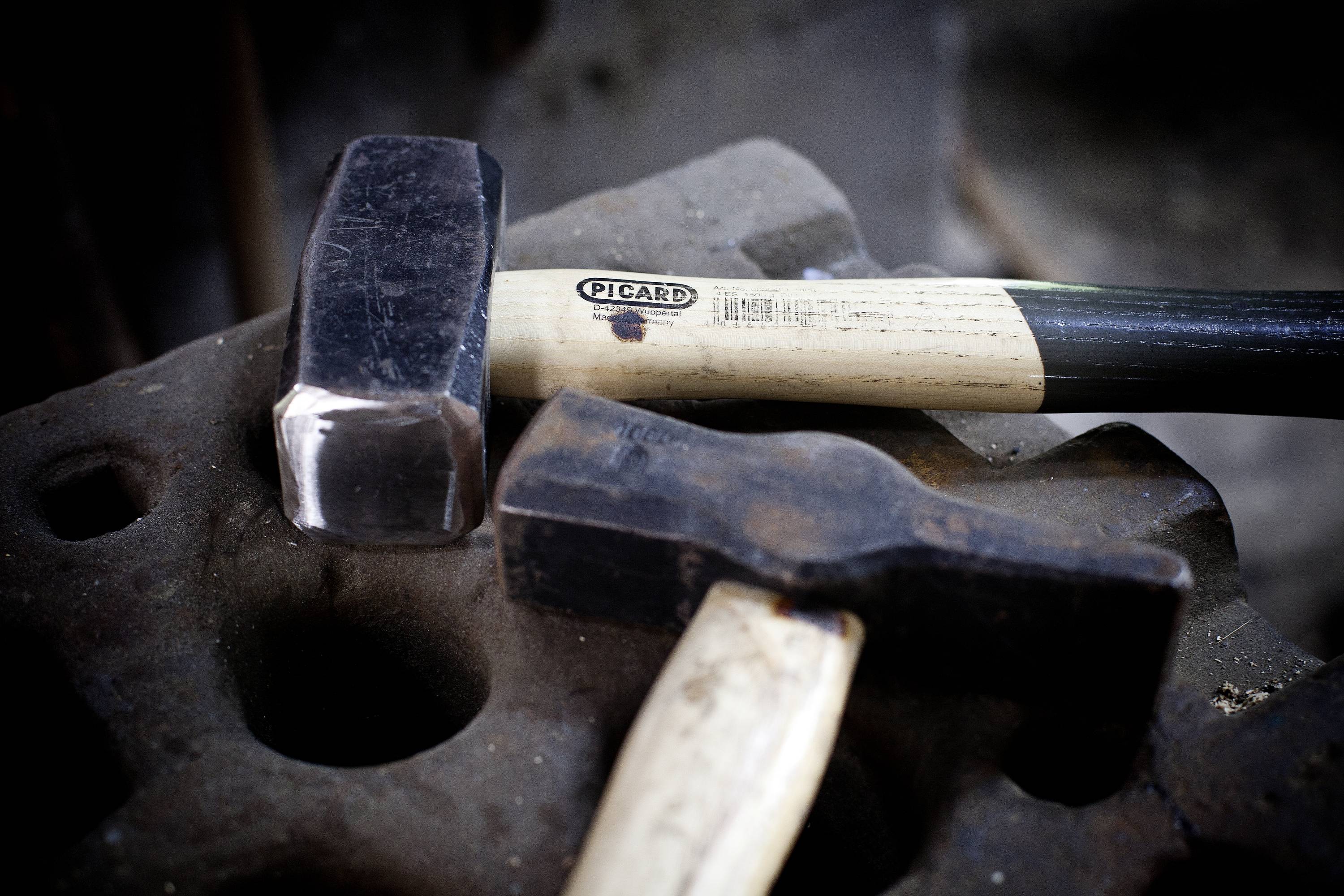 Un marteau neuf et un marteau usagé sont posés sur une enclume. Le marteau neuf porte une inscription 'Picard' sur le manche en bois.