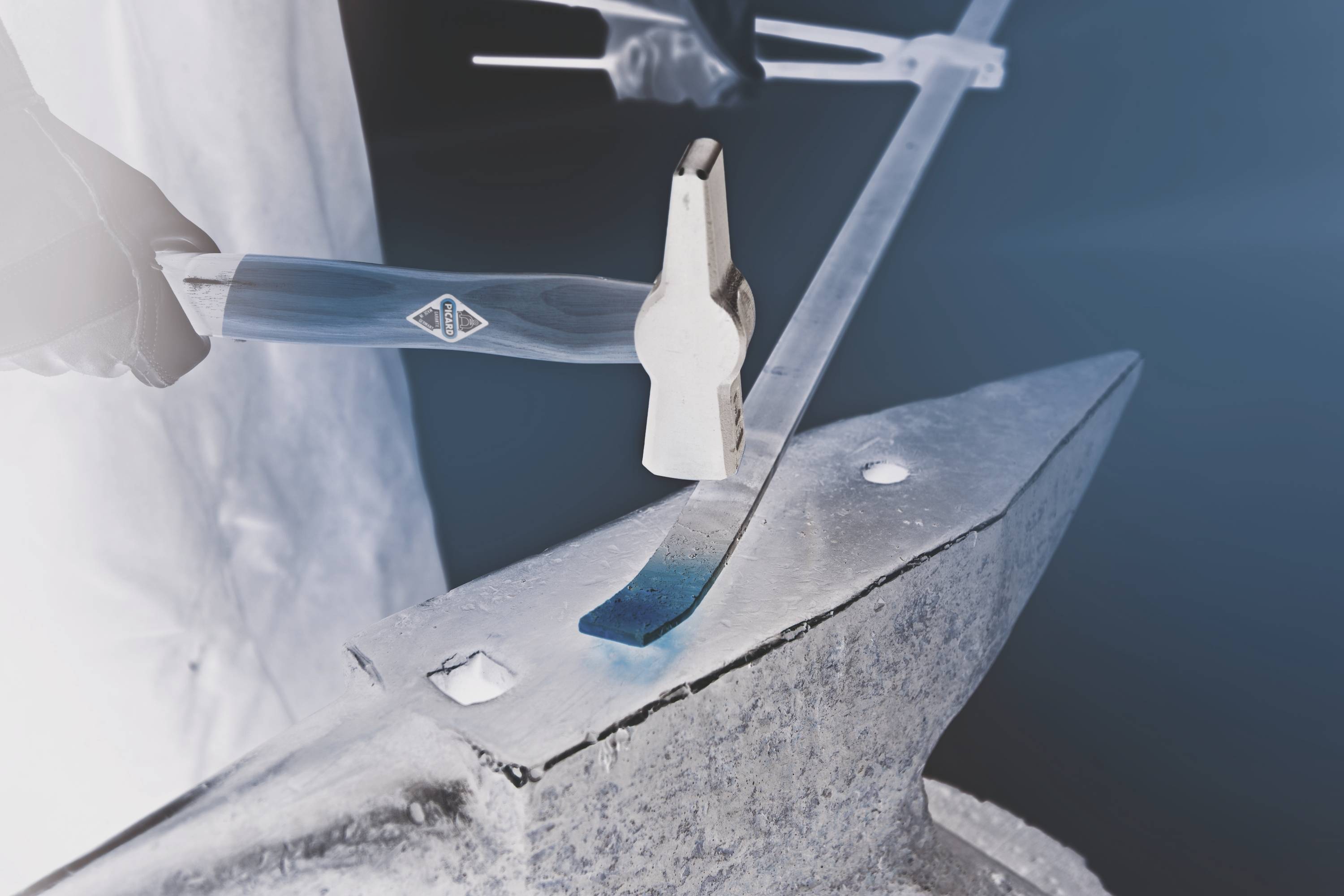 Un artisan forge un morceau de métal incandescent sur une enclume, marteau à la main, pour façonner le métal.