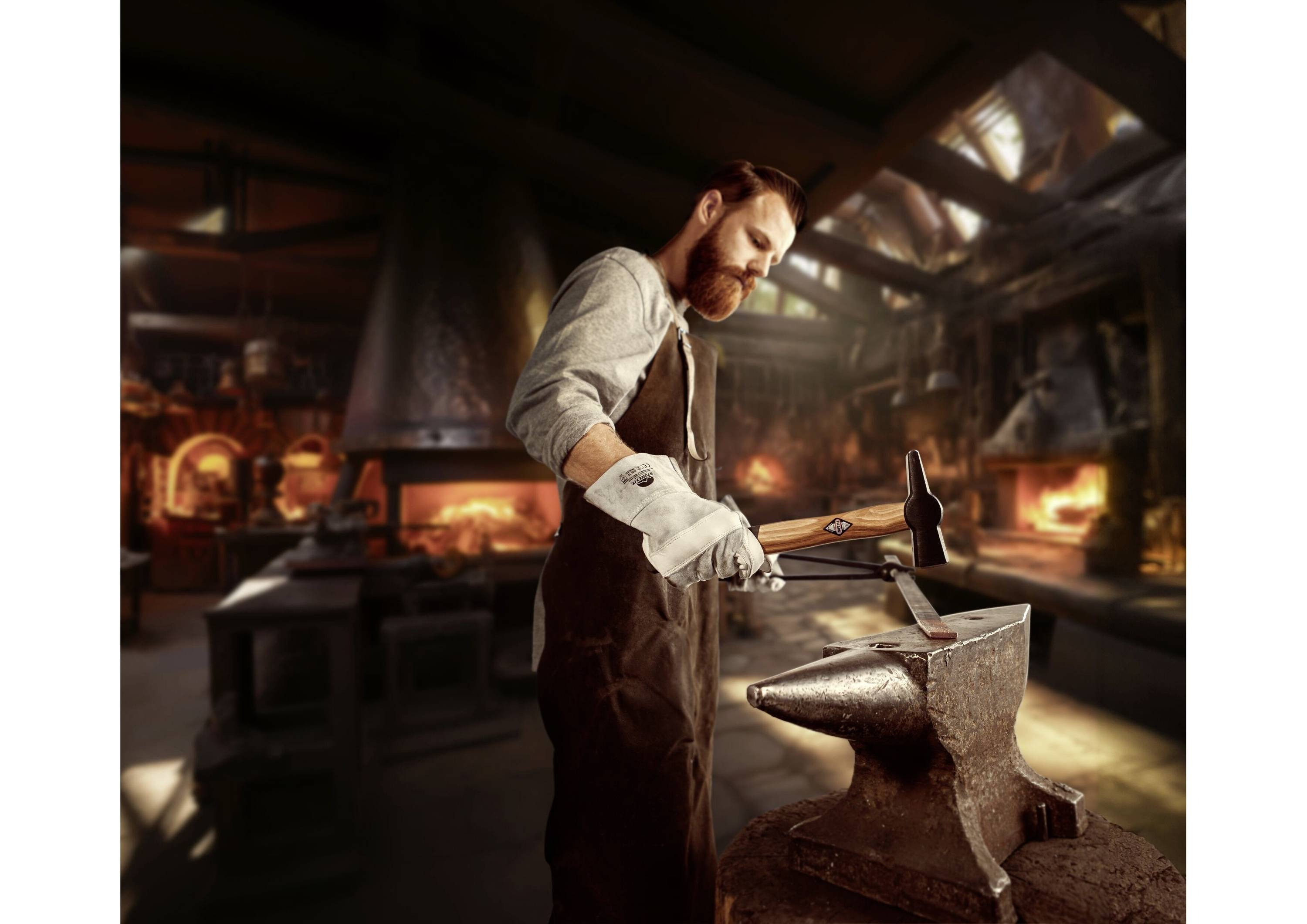 Un homme forge avec un marteau sur une enclume dans un atelier avec un four brûlant à l'arrière-plan.