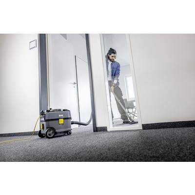 Un homme nettoie le sol moquetté d'un bureau avec un aspirateur. L'aspirateur est posé sur le sol et branché à une prise électrique.