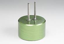 Condensateur électret cylindrique vert avec deux broches métalliques saillantes, placé sur un fond neutre.