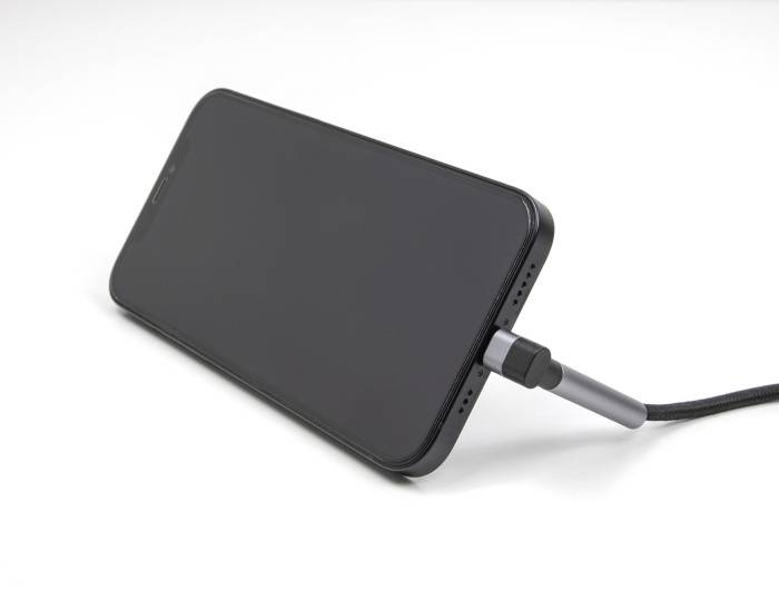 Un smartphone noir est posé sur une table et se charge via un câble USB. L'écran est éteint.