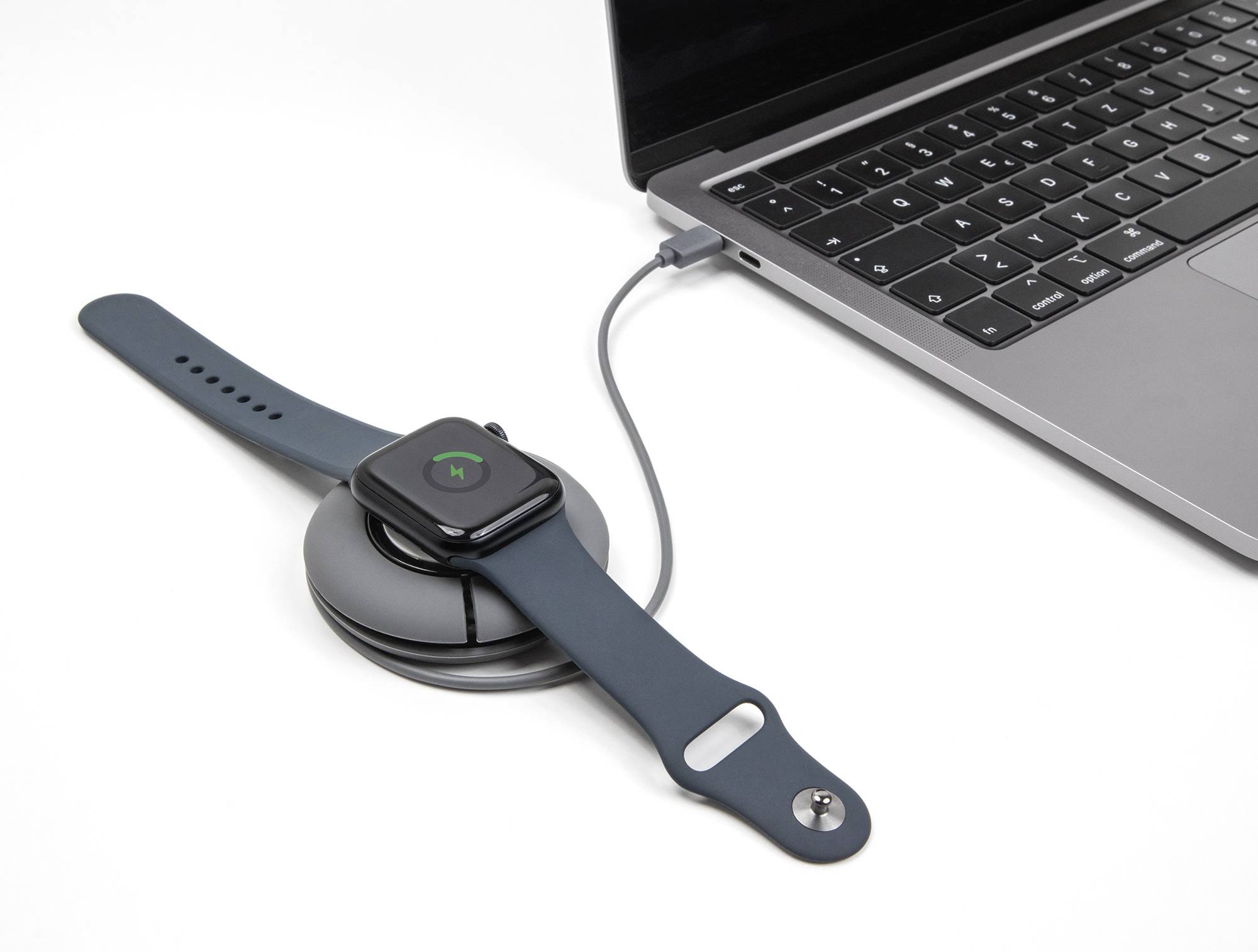 Une montre connectée est chargée à l'aide d'un câble USB sur un ordinateur portable. La montre affiche un symbole de charge sur son écran.
