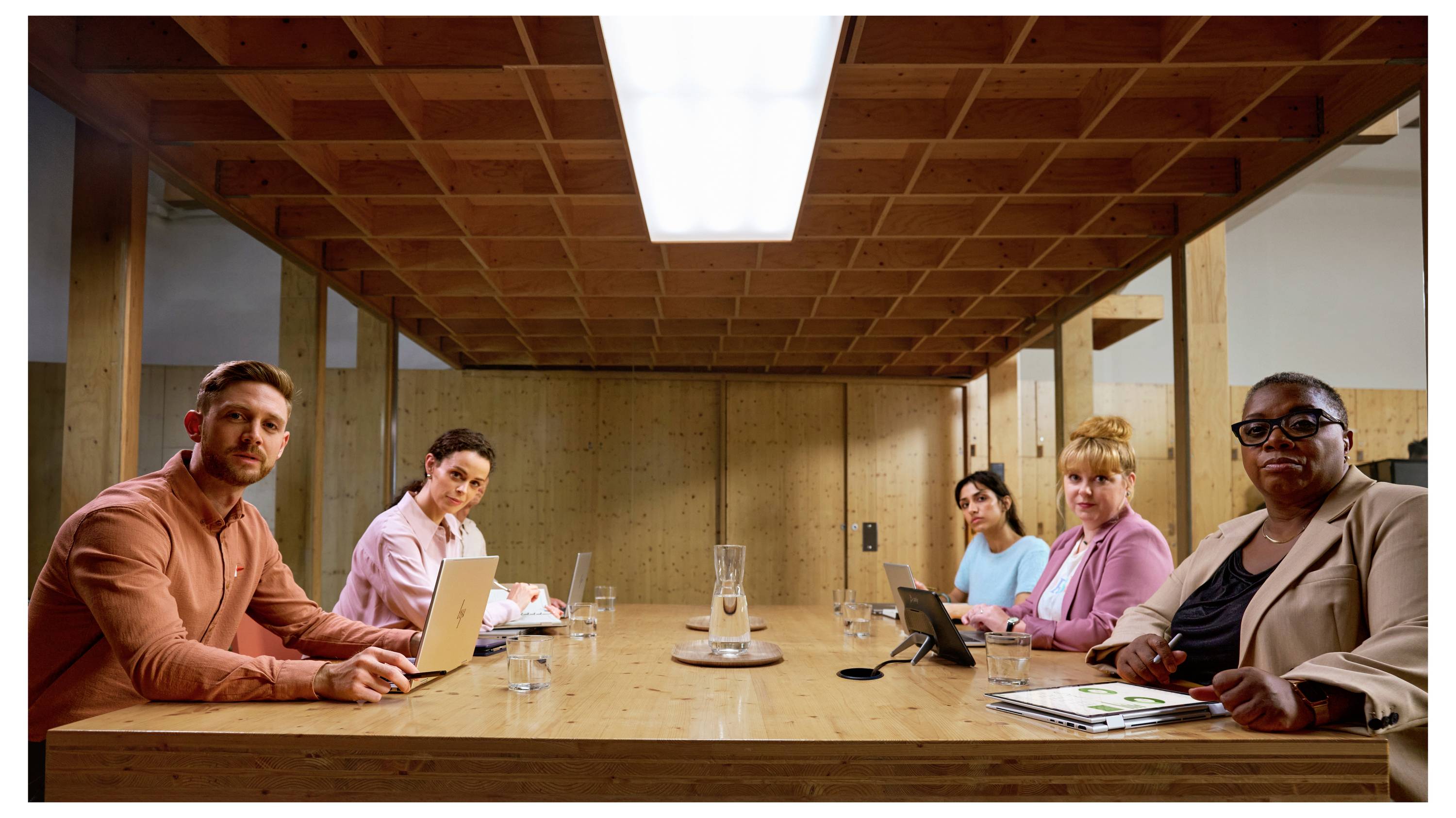 Six personnes sont assises autour d'une table de conférence dans un bureau moderne. Elles regardent attentivement en direction de la caméra.