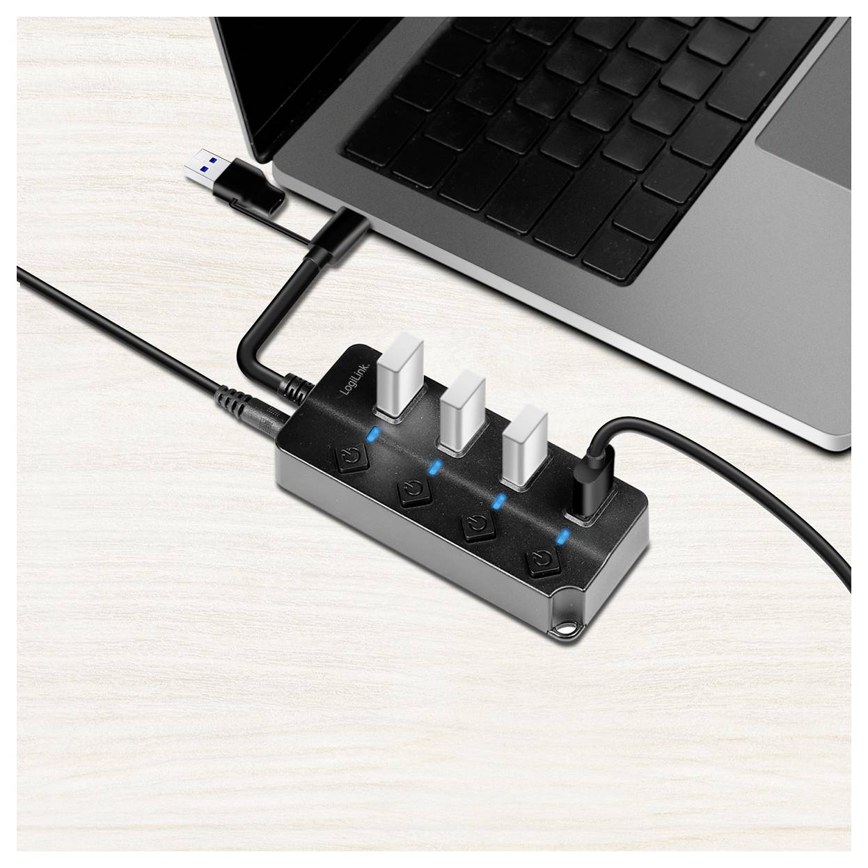 Un hub USB à quatre ports est connecté à un ordinateur portable. Trois des ports sont actifs et s'illuminent en bleu.