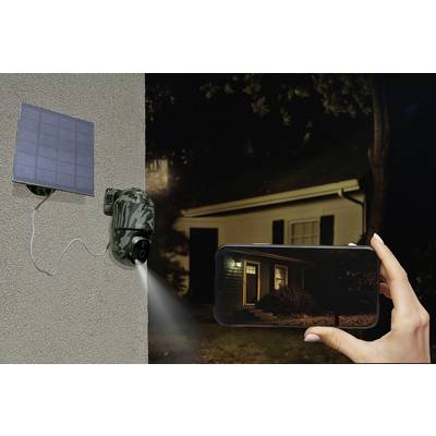 Une caméra de surveillance extérieure sur une maison transmet une vidéo en direct sur un smartphone. La caméra est équipée d'un panneau solaire, et il fait nuit.
