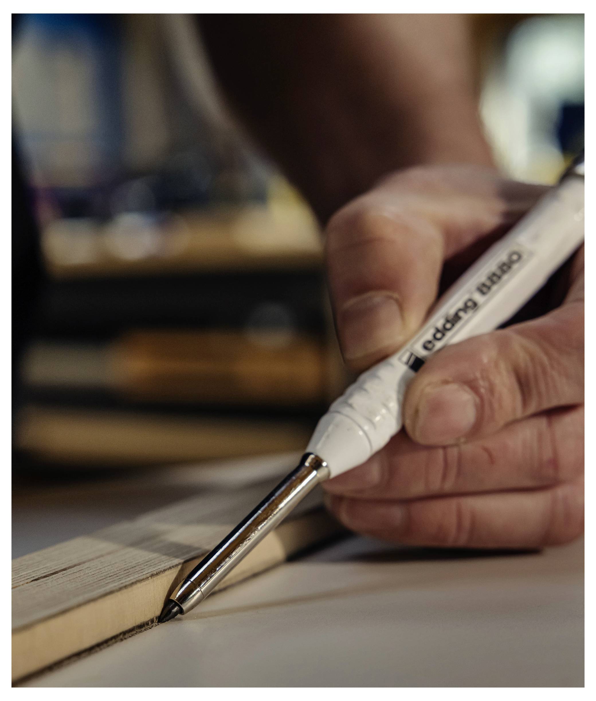 Gros plan d'une main utilisant un marqueur peinture blanc « edding 8880 » pour appliquer de la colle ou un adhésif le long du bord de papier ou de carton empilés.