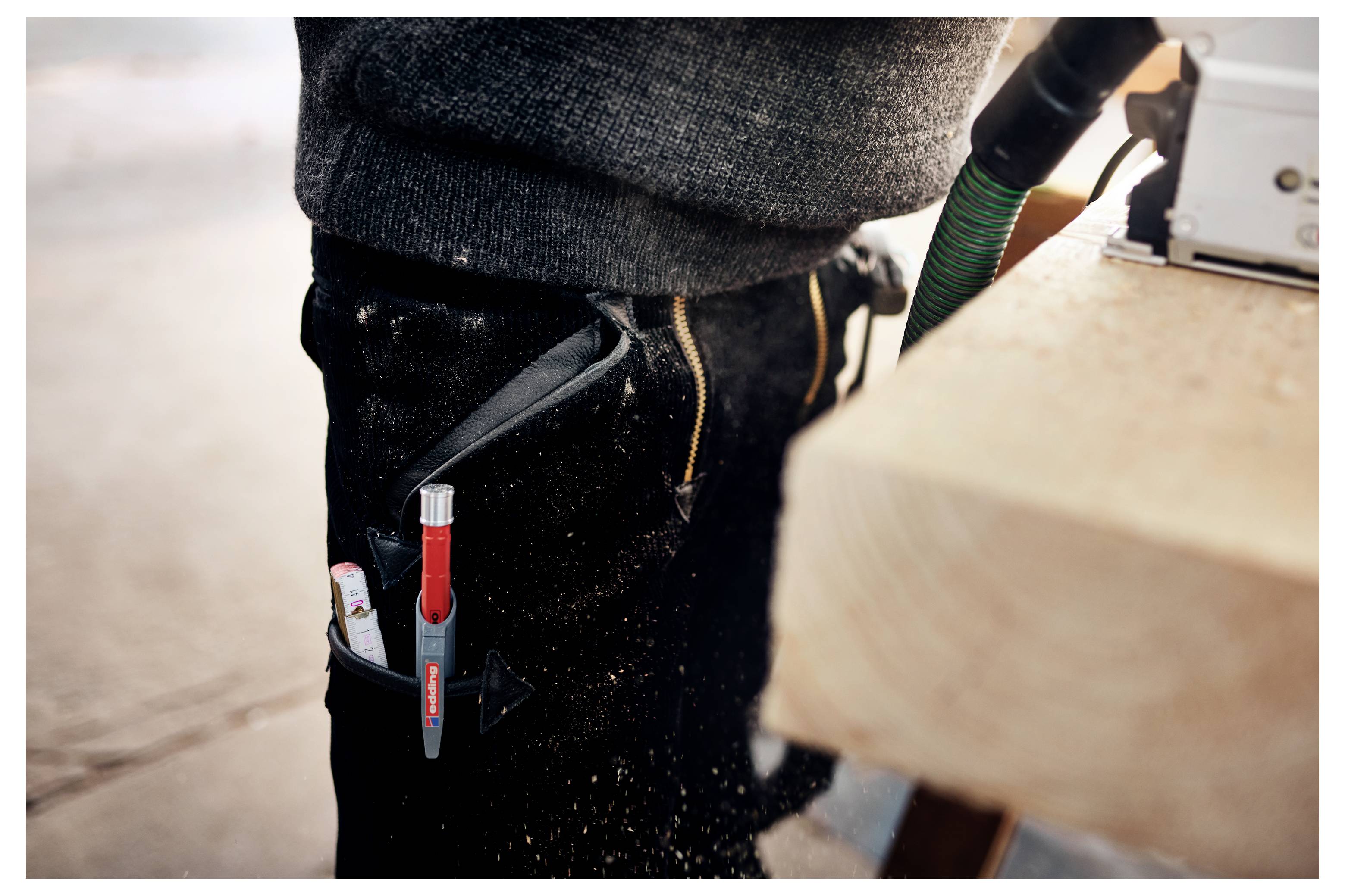 Gros plan d'un travailleur portant une ceinture à outils avec des stylos et un marqueur rouge en train d'utiliser un outil électrique sur une planche de bois.