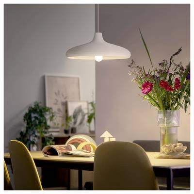 Salle à manger moderne avec une suspension blanche au-dessus d'une table dressée avec un livre ouvert et un vase de fleurs.